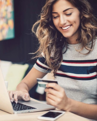 Eine junge Frau ist vor dem Laptop und benutzt ihre Debit- oder Kreditkarte fuer das Online-Shopping.